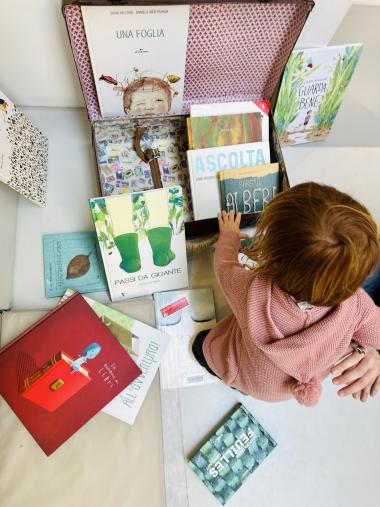 bambina piccola che guarda diversi albi illustrati in una valigia
